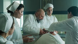 Der Ausschnitt aus der ARD Mini-Serie «Davos 1917» zeigt, wie mehre Ärtzte und Krankenschwestern in historischen Kostümen um einen OP-Tisch gebäugt sind.