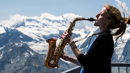 Eine Frau spielt Saxophon vor einer Bergkulisse