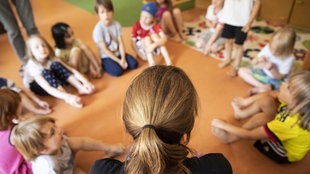 Eine Erzieherin sitzt mit Kinder in der Kita auf dem Boden.