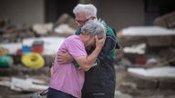 Zwei Männer liegen sich verzweifelt in den Armen im Hintergrund die Zerstörung der Flutkatastrophe, Archivbild: Ahrtal 19.07.2021