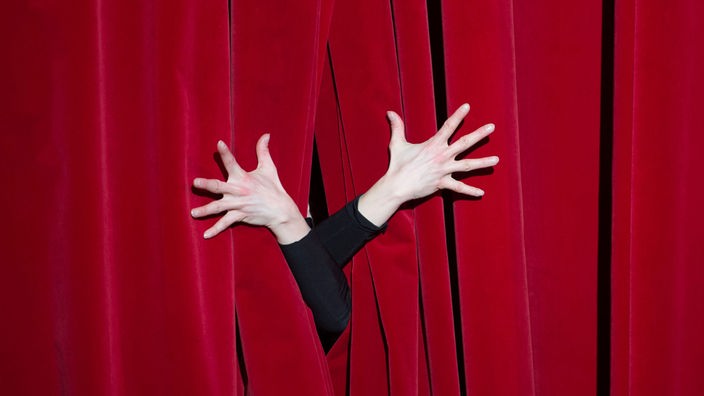 Hände auf einem roten Theatervorhang, Symbolbild