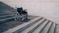 Symbolfoto zum Thema: Rollstuhl und Barrierefreiheit. Ein Rollstohl steht auf einem Treppenabsatz