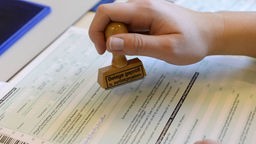 Eine Hand stempelt ein deutsches Steuerformular: "Belege geprüft und zurückgegeben"