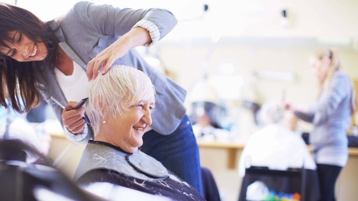 Friseurin schneidet Kundin die Haare, beide lächeln. 