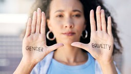 Eine Frau mit schwarzem, gelocktem Haar hällt ihre Hände in die Kamera - darauf stehen die Worte "Gender" und "Equality".