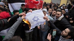 Teilnehmer einer Demonstration verbrennen eine selbstgemalte Fahne mit einem Davidstern im Stadtteil Neukölln.