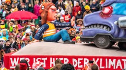 Motivwagen im Düsseldorfer Karneval von Wagenbauer Jacques Tilly: Klimaaktivisten der Letzten Generation blockieren einen qualmenden LKW