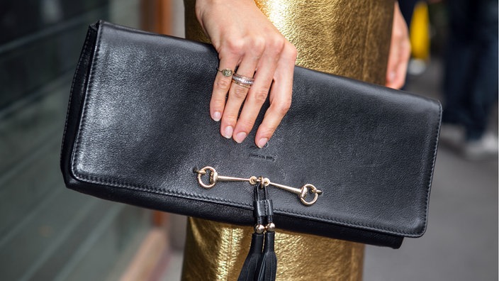 Nahaufnahme einer Person in einem goldenem Kleid, die in ihrer Hand eine teure Lederhandtasche hält.