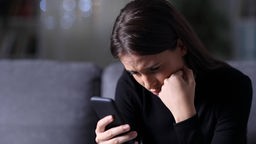 Symbolbild zur Flut schlechter Nachrichten: Eine Frau schaut besorgt auf ihr Smartphone