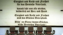  Text des Deutschlandliedes auf einer Wand, vorne leere Stühlen