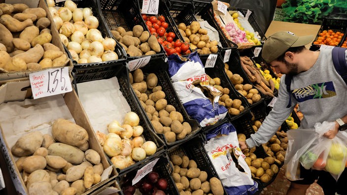Ein Mann packt Gemüse von der Auslage eines Supermarkts in einen Plastikbeutel.