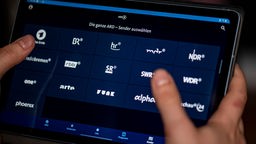 Ein Mann benutzt die ARD-Mediathek App auf einem Tablet, auf dem unter anderem die Sender BR, hr, mdr, NDR, phoenix, rbb, SR, SWR, WDR und arte zu sehen sind.