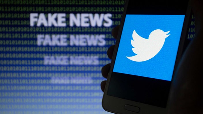 Logo-Symbol von Twitter ist auf einem Smartphone-Bildschirm vor dem  Text  "FAKE NEWS" zu sehen. 