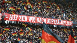 In einem mit Zuschauern gefülltem Fußballstadion hängt ein Banner mit dem Schriftzug "AUF ZUR WM NACH AUSTRALIEN 2023".