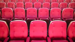 Rote Sessel stehen in einem Kinosaal. 