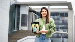 Linda Zervakis präsentiert den Avatar "KI-Linda" auf einem Smartphone. 