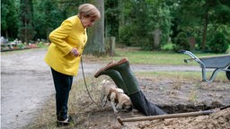 Angela (Katharina Thalbach) und Mops "Helmut" finden die Leiche in einer Szene aus "Miss Merkel - Ein Uckermark-Krimi: Mord auf dem Friedhof", 14.03.2024.