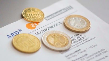 Geldmünzen liegen auf einem Schreiben zum Beitragsservice.