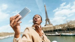 Eine Frau macht ein Selfie mit dem Eiffelturm im Hintergrund.