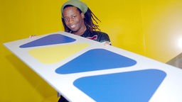 Mola Adebisi, ehemaliger Viva-Moderator, hält im Sendegebäude das bekannte Logo des Musiksenders in Händen, 10.11.2023.