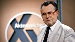 Eduard Zimmermann steht im September 1986 neben dem Logo der Sendung "Aktenzeichen XY ungelöst"