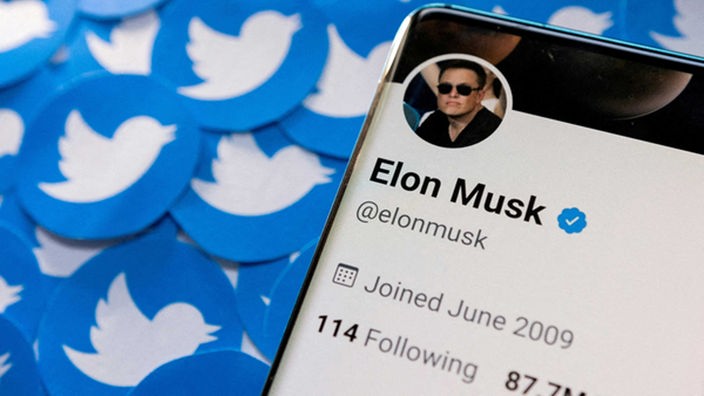 Abbildung zeigt das Twitter-Profil von Elon Musk auf dem Smartphone und gedruckte Twitter-Logos.