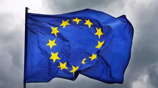 EU-Flagge weht vor dunklem Himmel. 