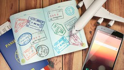 Reisepass mit Visa und Bordkarten, Flugzeug und Handy liegen auf einem Holztisch.