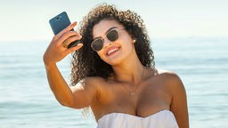 Junge Frau macht ein Selfie am Strand. 