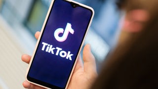 Ein Mädchen hält ihr Smartphone in den Händen, auf dem sie ein Foto der Kurzvideo-App TikTok geöffnet hat.