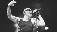 Schwarzweiß-Foto des Sängers Willi Resetarits, der mit Sonnenbrille und Unterhemd auf der Bühne ins Mikrofon singt