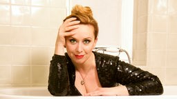 Die Kabarettistin Martina Brandl lehnt über einer Badewanne