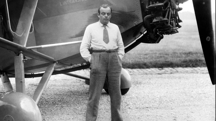 Schwarz-Weiß-Aufnahme: Mann posiert vor einem Flugzeug