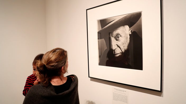 Eine Frau mit Kind auf dem Arm betrachtet eine Porträtfoto von Pablo Picasso, das Irving Penn gemacht hat