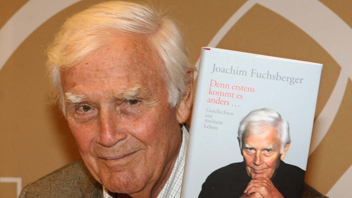 Jochim Fuchsberger hält sein Buch "Denn erstens kommt es anders..." in der Hand