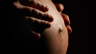Eine hochschwangere Frau fasst sich mit beiden Händen an ihren Bauch