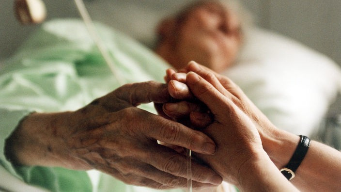 Eine Krankenschwester hält die Hand einer sterbenskranken Patientin