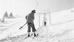 Ein Skifahrer fährt mit dem Skilift den Hang hinauf