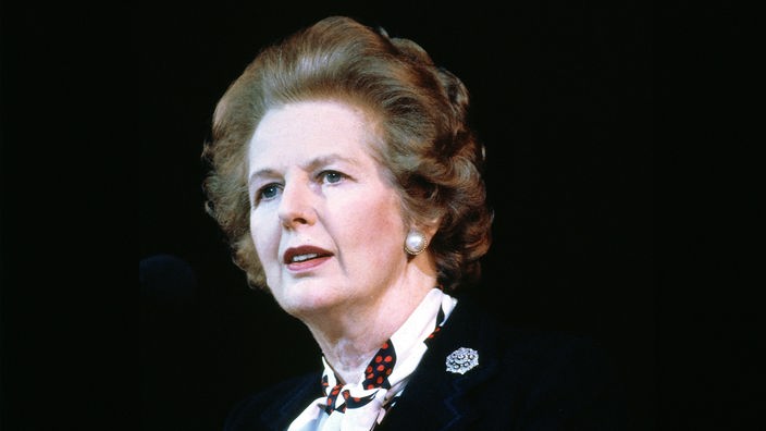 Margaret Thatcher im Porträt - sie schaut mit perfekt frisierten Haaren ernst zur Seite, der Hintergrund ist schwarz, Aufnahme von 1980