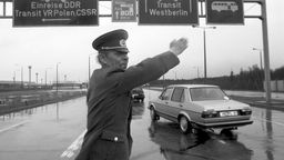 DDR-Grenzbeamter winkt bei Grenzübergang Marienborn Autos durch