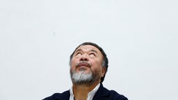 Ai Weiwei, ein Mann mit rundlichem Gesicht, weißmeliertem Vollbart und kurzen Haaren schaut auf einer Porträtaufnahme nach oben