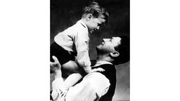Ein Mann hält seinen kleinen Sohn so auf dem Arm, dass der Junge von oben auf ihn schaut, der Mann strahlt den Jungen glücklich an