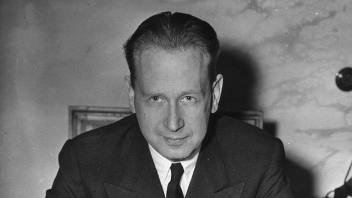 Dag Hammarskjöld sitzt an einem Schreibtisch und schaut in die Kamera.