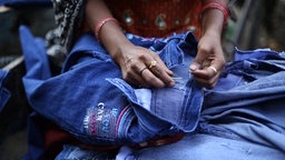 Eine Frau näht an einer Jeans mit der Aufschrift "If you can catch me" in dem Slum Shastri Park am Fluß Yamuna im Osten von Delhi, Indien