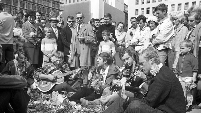 Hippies spielen am 08.09.1967 Gitarre auf der Straße in Essen, Passanten stehen drumherum