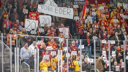 DEG-Fans halten in Gedenken bei einer Schweigeminute für den verstorbenen Eishockyprofi Tobias Eder von den Eisbären Berlin dessen Rückennummer hoch.