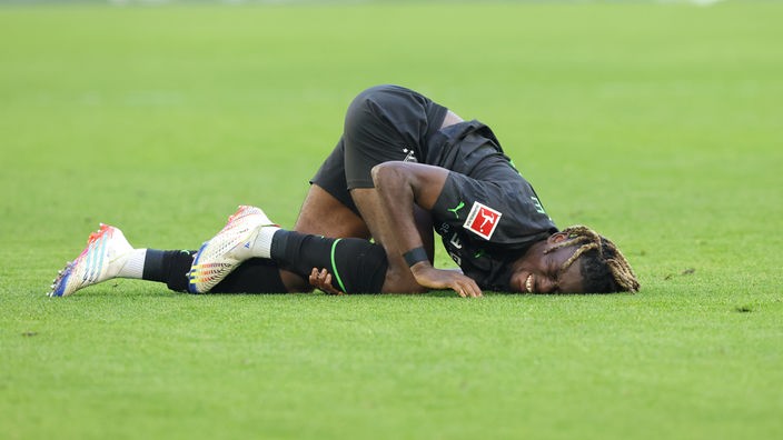 Fußballprofi Manu Koné (Borussia Mönchengladbach) liegt mit schmerzverzerrtem Gesicht am Boden