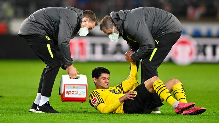 Mahmoud Dahoud von Borussia Dortmund liegt verletzt am Boden und die Betreuer helfen ihm auf die Beine