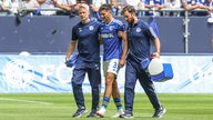 Schalke-Verteidiger Leo Greiml (Mitte) wird nach seiner Verletzung vom Platz begleitet