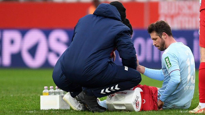 Mark Uth (r.) vom 1. FC Köln sitzt auf dem Spielfeld und wird behandelt